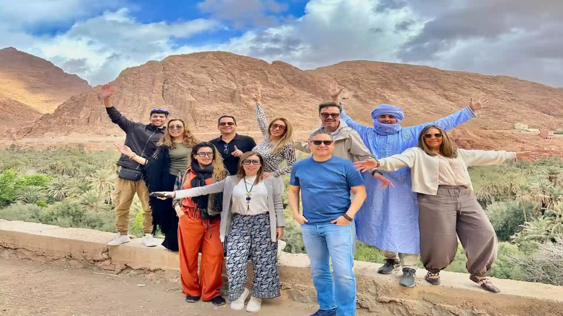 Happy group of travelers posing with a local guide at Todra Gorge palm oasis during a two weeks in Morocco itinerary