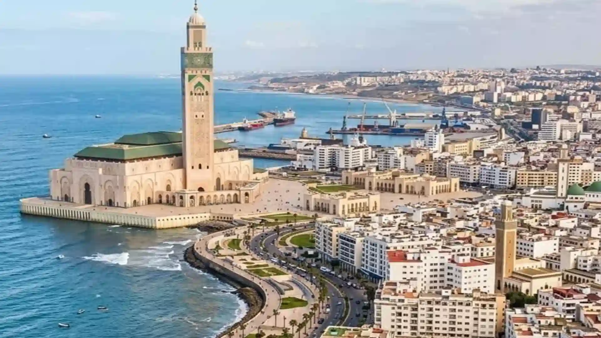 High-angle aerial view of the Hassan II Mosque standing along the turquoise Atlantic Ocean with the Casablanca cityscape in the background. things to do in Casablanca
