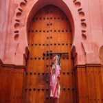 Female traveler standing in front of a massive, intricately carved wooden archway door in Marrakech