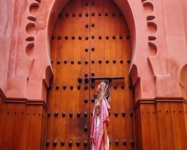 Female traveler standing in front of a massive, intricately carved wooden archway door in Marrakech