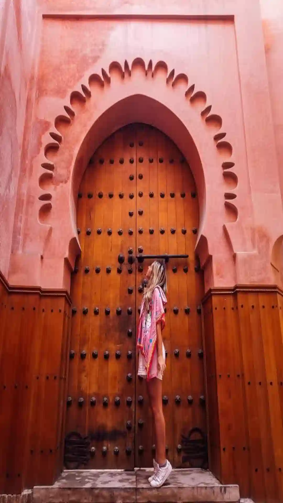 Female traveler standing in front of a massive, intricately carved wooden archway door in Marrakech