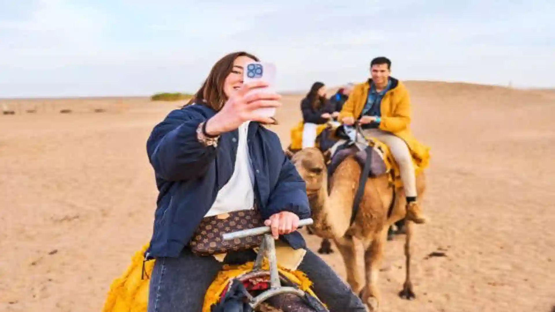 A woman taking a selfie with her smartphone while riding a camel across the Sahara desert in Morocco eSIM.